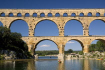 Pont du Gard.  Central view of Roman aqueduct from west side in evening light with three tiers of continuous arches and canoe heading east on water below.  Bridge arch European French Western Europe...