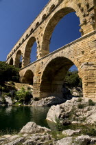 Pont du Gard.  Angled view of three tiers of arches from the west side in glowing evening light.  Large rocks extending from bank in the foreground.Bridge arch Roman aqueduct European French Western...