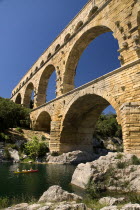 Pont du Gard.  Angled view of three tiers of arches from the west side in glowing evening light with large rocks extending from bank in the foreground.Bridge arch Roman aqueduct European French Weste...