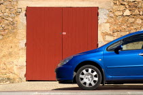 Roussillon.  Blue car parked outside red painted doorway set into exterior wall of one of the red stone buildings of the town.European French Western Europe 1 Automobile Automotive Cars Motorcar Sing...