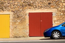 Roussillon.  Blue car parked outside red stone building with red and yellow painted double doorways.European French Western Europe 1 Automobile Automotive Cars Motorcar Single unitary Automobiles Aut...