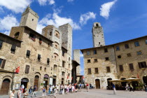 Tourists in Piazza della Cisterna lined with shops and ringed by five of the medieval towers under a blue skyEuropean Italia Italian Southern Europe Toscana Tuscan 5 History Holidaymakers Tourism