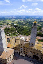 View of the Palazzo Vecchio del Podesta of 1239 with its medieval tower and tourists in the Piazza del Duomo with rooftops and Tuscan farmland on the slopes of the hill townEuropean Italia Italian So...