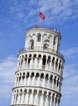 The Campo dei Miracoli or Field of Miracles.The Leaning Tower or Torre Pendente belltower with tourists on the top level beside the red flag with a white cross the emblem of Pisa under a blue skyEuro...