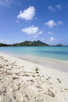 West Indies, Caribbean, Grenada, Carriacou, The calm clear blue water breaking on Paradise Beach in L'Esterre Bay with Point Cistern and The Sister Rocks in the distance.