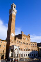 he Torre del Mangia campanile belltower and facade of the Palazzo Publico town hall in the Piazza del Campo under a blue sky with tourists in the squareEuropean Italia Italian Southern Europe Toscana...