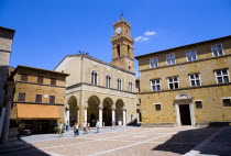 Val D Orcia Piazza Pio II with Palazzo Communale Town Hall with its campanile belltower and Palazzo Borgia on the right. Tourists walking in the square under a blue skyEuropean Italia Italian Souther...