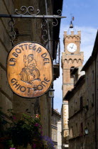 Val D Orcia Sign for la Bottega Ghiottone wine bar hanging from a wall in a street with the campanile belltower of Palazzo CommunaleEuropean Italia Italian Southern Europe Toscana Tuscan Inn Pub Tave...