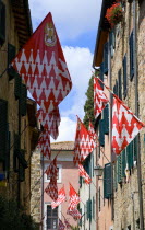 Narrow street with shuttered windows. Red and white flags of the Castello Quartieri or quarter of the medieval town decorate the street during the Festival of BarbarossaEuropean Italia Italian Southe...