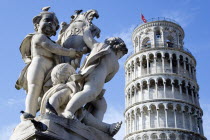 Campo dei Miracoli or Field of Miracles Marble statue of three cherubs holding a shield in front of the Leaning Tower belltower or Torre Pendente under a blue skyEuropean Italia Italian Southern Euro...