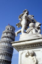 Campo dei Miracoli or Field of Miracles Marble statue of three cherubs holding a shield in front of the Leaning Tower belltower or Torre Pendente under a blue skyEuropean Italia Italian Southern Euro...