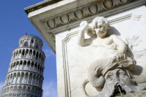 Campo dei Miracoli or Field of Miracles Carving of a cherub and bearded male face on a water fountain in front of the Leaning Tower belltower or Torre Pendente under a blue skyEuropean Italia Italian...