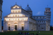 Campo dei Miracoli or Field of Miracles The Duomo Cathedral and Leaning Tower belltower or Torre Pendente illumunated at dusk with tourist sitting on the grass and walking at their baseEuropean Itali...