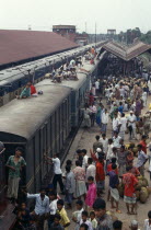 Train loaded with passengers in station with crowds on the platform and people sitting on the train roof.Asia Asian Bangladeshi Asia Asian Bangladeshi