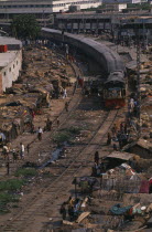 Train travelling through Tejgoan slum with ramshackle dwellings beside tracks and people living amongst rubbish and polluted water.shanty town poor poverty homes houses Asia Asian Bangladeshi Dacca E...