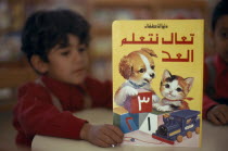 School boy reading a colourful book illustrated with a kitten and puppy al-Kuwayt Colorful Kids Kuwaiti Learning Lessons Middle East Teaching al Kuwayt