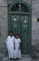Two boys wearing long white robes standing outside a green doorway2 al-Kuwayt Kids Kuwaiti Middle East Religious al Kuwayt Religion