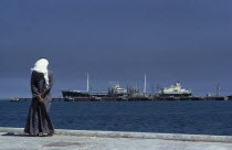 Man wearing a white headscarf looking out across the sea towards the Mina Ahmadi oil terminalal-Kuwayt Kuwaiti Middle East One individual Solo Lone Solitary 1 al Kuwayt Male Men Guy Religious Salt Wa...
