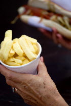 Findon village Sheep Fair Elderly lady holding a polystyrene mug full of potato fries in one hand and a hot dog with tomato ketchup and onions in the other.Great Britain Northern Europe UK United Kin...