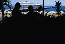 Tourists in the Cruise Ship Terminal looking out through the glass window towards the Queen Mary 2 liner moored offshore.Caribbean Destination Destinations Grenadian Greneda West Indies Grenada Holid...