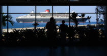 Tourists in the Cruise Ship Terminal looking out through the glass window towards the Queen Mary 2 liner moored offshore.Caribbean Destination Destinations Grenadian Greneda West Indies Grenada Holid...