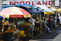 Busy fruit and vegetable stalls under umbrellas in Market Square outside Foodland supermarket.Caribbean Destination Destinations Grenadian Greneda West Indies Grenada