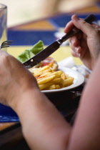 Sunburnt white caucasian woman eating a plate of potato chips and tomato ketchup with a knofe and fork.Caribbean Destination Destinations Grenadian Greneda West Indies Grenada Crisps Female Women Gir...