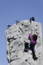 Young girl climbing manmade rockface using safety harness.American childrenchildkidkidsplayplayingplayfulchildhoodyoungyouthgirlgirlsyoungschoolageelementaryfunhappyhappinesspeople...