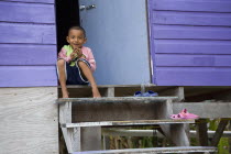 A young Belizean boy is sitting down at the doorstep of his purple colored wooden house.SummerHolidaysVacationRelaxSunTropicalTourismHotHeatStyleHappyExpressionFaceEthnicEthnicityFolkl...