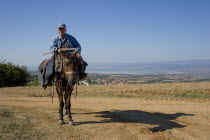Petrokerasa. Greek farmer on his horse and their shadow  at the Greek countryside with a village and a lake noticeable at the background.Horse ridingFace portraitElderlyThird AgeVillage peopleTr...