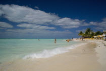 Isla Mujeres exotic tropical beach with blue-sky and white clouds and three people ready to swim at the crystal clear seawater while others are walking by the coastline or relaxing at the sun beds und...