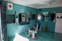 Interiors of an old style barber shop with noticeable the old chair  the green colored walls and floor  the big first aid box with the red cross on it and the strong sunlight coming from the door.Hai...
