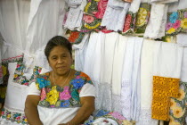 Plaza Principal. Portrait of a Mexican woman selling traditional Yucatan areas white dresses and fabrics with colored flowers while she is wearing one of them herself and is looking directly at the le...