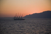 Sun sets behind four masted Schooner with silhoetted coast of Nisyros to right on ferry route between Rhodes and Kos.Greek islandsDodecaneseRhodesRhodosRodiAegeanMediterraneanEuroholidayUNES...