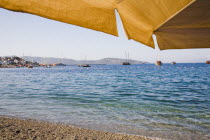 View across bay towards gulf of Gokova from beach beneath yellow parasols with lines of yachts and Gulet boats. Turkish Aegean coastmediterraneanresortformerly HalicarnassusHalikarnasregion of C...