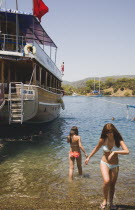 Young  Turkish women holidaymakers in bikinis in shallow water beside boat moored off Gemiler also known as St Nicholas Island.Fethiyeformerly Telmessosformerly modern Greek MakriAegeanTurkish ri...