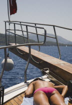 Female tourist sunbathes topless on prow of Turkish pleasure boat in late afternoon sun.Fethiyeformerly Telmessosformerly modern Greek MakriAegeanTurkish rivieraSaint Nicholas LycianLyciaNicho...