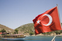 Turkish flag on yacht with day trip pleasure boat in bay beyond.Fethiyeformerly Telmessosformerly modern Greek MakriAegeanTurkish rivieraLycianLyciasummerseasonsuntouristholidaycruisesea...