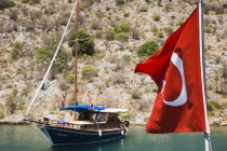 Turkish flag in foreground of Gulet boat moored in bay beyond.Fethiyeformerly Telmessosformerly modern Greek MakriAegeanTurkish rivieraLycianLyciasummerseasonsuntouristholidaycruiseseac...