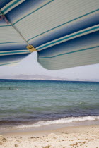Tingaki beach on North East coast facing Turkey and Bodrum area from shade of blue and white parasol and sunbed with clear bathing beach and water.Greek Islands Tingaki Resort Summer Clear Blue Sky e...