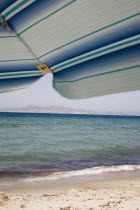 Tingaki beach on North East coast facing Turkey and Bodrum area from shade of blue and white parasol and sunbed with clear bathing beach and water.Greek Islands Tingaki Resort Summer Clear Blue Sky e...