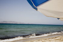 Tingaki beach on North East coast facing Turkey and Bodrum area from shade of blue and white parasol and sunbed with clear bathing beach and water.Greek Islands Tingaki Resort Summer Clear Blue Sky e...