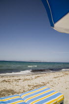 Tingaki beach on North East coast facing Turkey and Bodrum area from shade of blue and white parasol and sunbed with clear bathing beach and water.Greek Islands Tingaki Resort Summer Clear Blue Sky e...