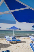 Tingaki beach on North East coast facing Turkey and Bodrum area from shade of blue and white parasol and sunbed with clear bathing beach and water.Greek Islands Tingaki Resort Summer Clear Blue Sky e...