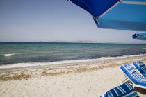 Tingaki beach on North East coast facing Turkey and Bodrum area from shade of blue and white parasol and sunbed with clear bathing beach and water.Greek Islands Tingaki Resort Summer Clear Blue Sky e...