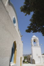 Agia Paraskevi Greek Orthodox Church.  Angled view of white exterior facade with pale blue and yellow painted window recesses and free standing white bell tower.Destination Destinations Ellada Europe...