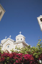 Agia Paraskevi Greek Orthodox Church.  Part view of white and cream facade against clear blue sky above dark pink flowering plant.Greek IslandsAegeanMediterraneanKossummerseasonholidayDestinat...