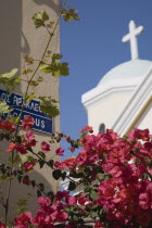 Iracleous Place street sign on corner of building opposite partly seen Agia Paraskevi Greek Orthodox church in Kos Town with dark pink bougainvillea in foreground.Greek Islands clear blue skysummer...