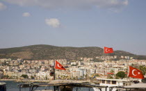 Turkish flags flying from cruise boats in foreground with town spread across coastal hillside beyond.TurkishAegeancoastresortsummersunshineearly summer seasonMediterraneanholidayDestination...