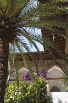 Architectural detail of building with timber framed overhanging roof and arched windows  palm tree and purple bougainvillea.TurkishAegeancoastresortsummersunshineearly summer seasonMediterrane...